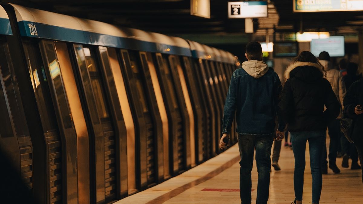 A couple walking on a subway platform with a train in the station.